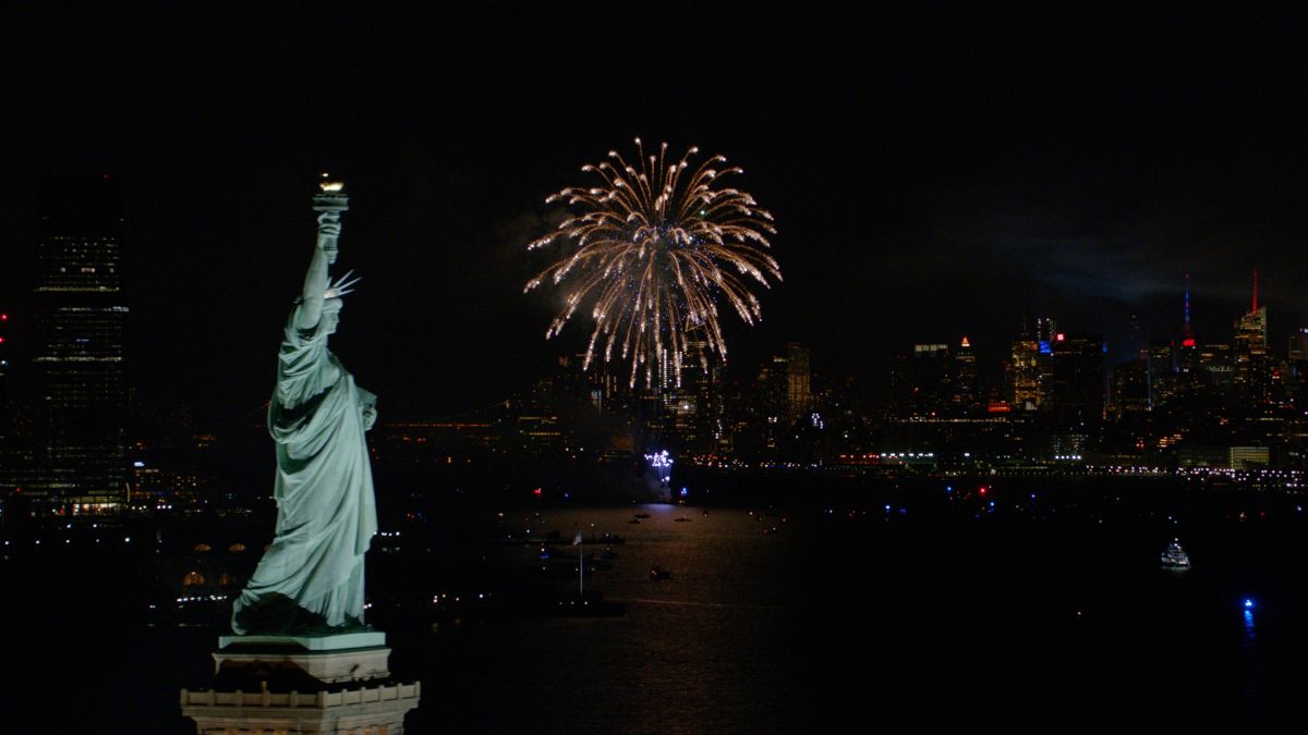 Overhead shot of the Statue of Liberty with a fireworks show lighting the sky in the background.