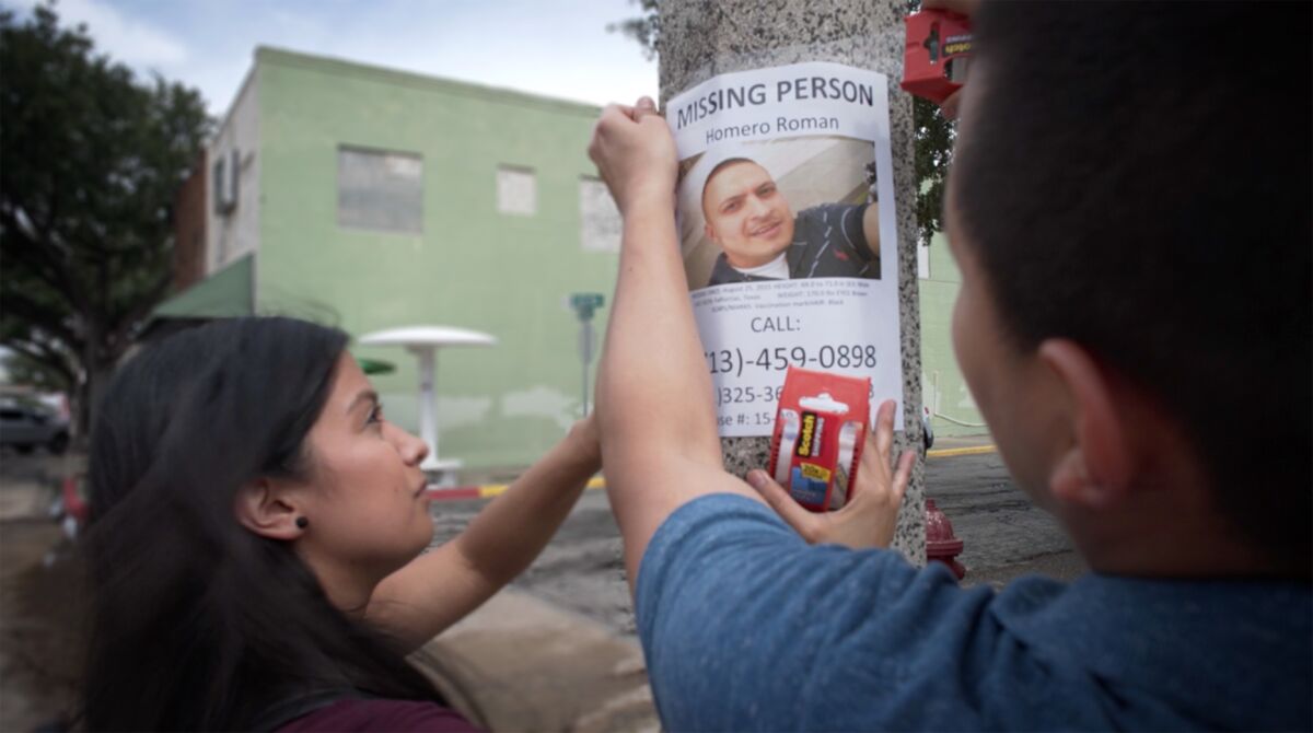 Woman hanging up missing person poster on lamp post