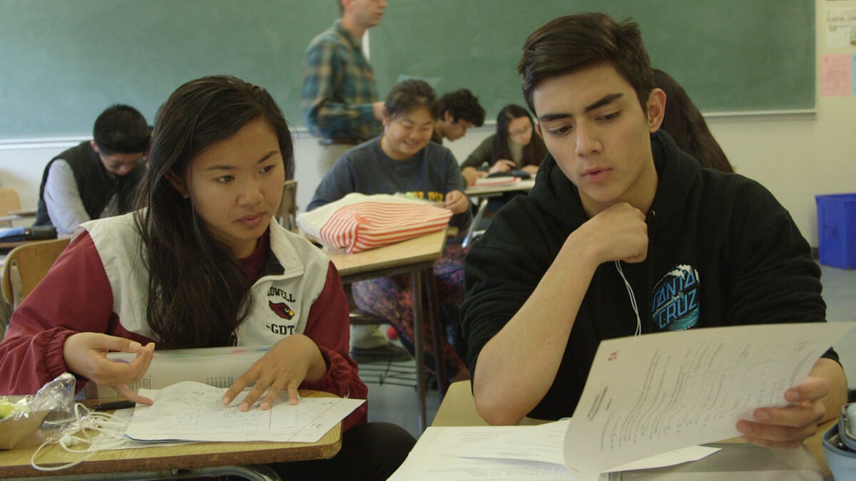 High school age girl and boy looking at piece of paper in classroom.