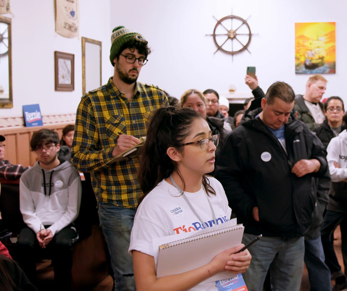 Many people in a room paying attention to a Latina caucus leader during the Iowa Caucuses in 2020.