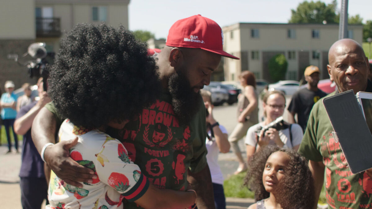 Michael Brown Senior is at the center of this photo mourning and celebrating the life of his son Michael, wearing red St Louis Cardinals hat.