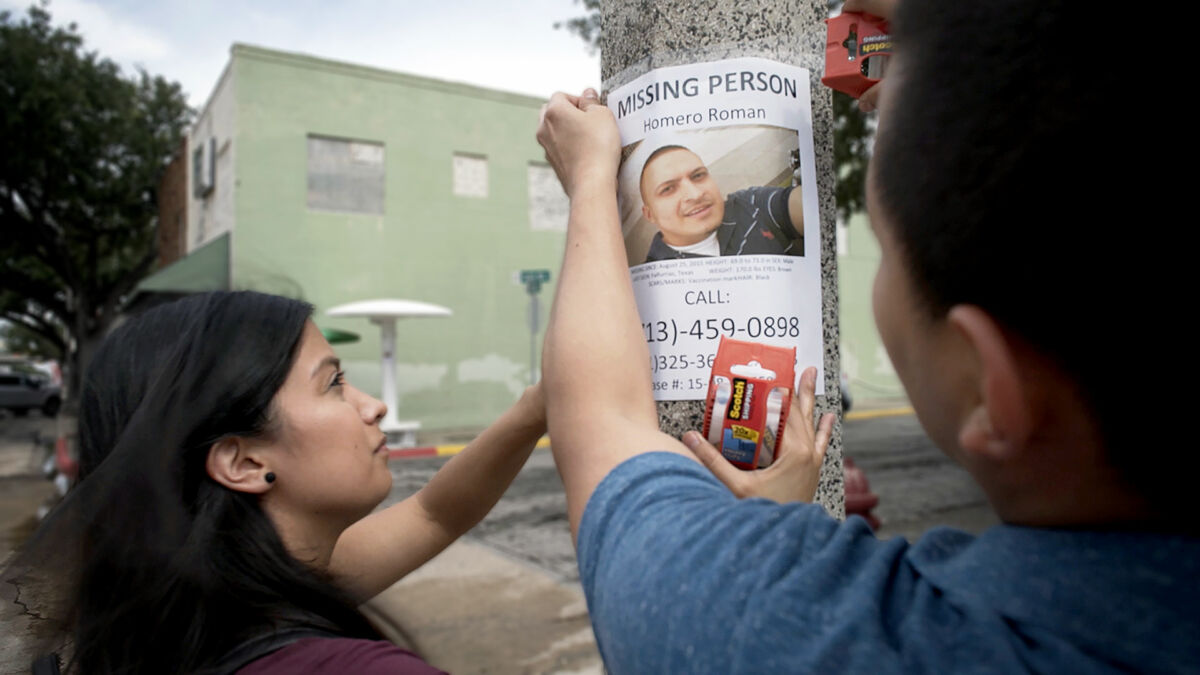 A husband and wife tape a missing persons poster to a telephone pole.