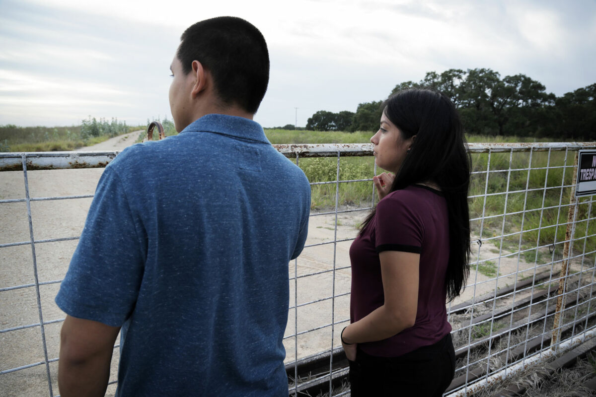 A husband and wife look over a fence straddling a river in Brooks County, Texas.