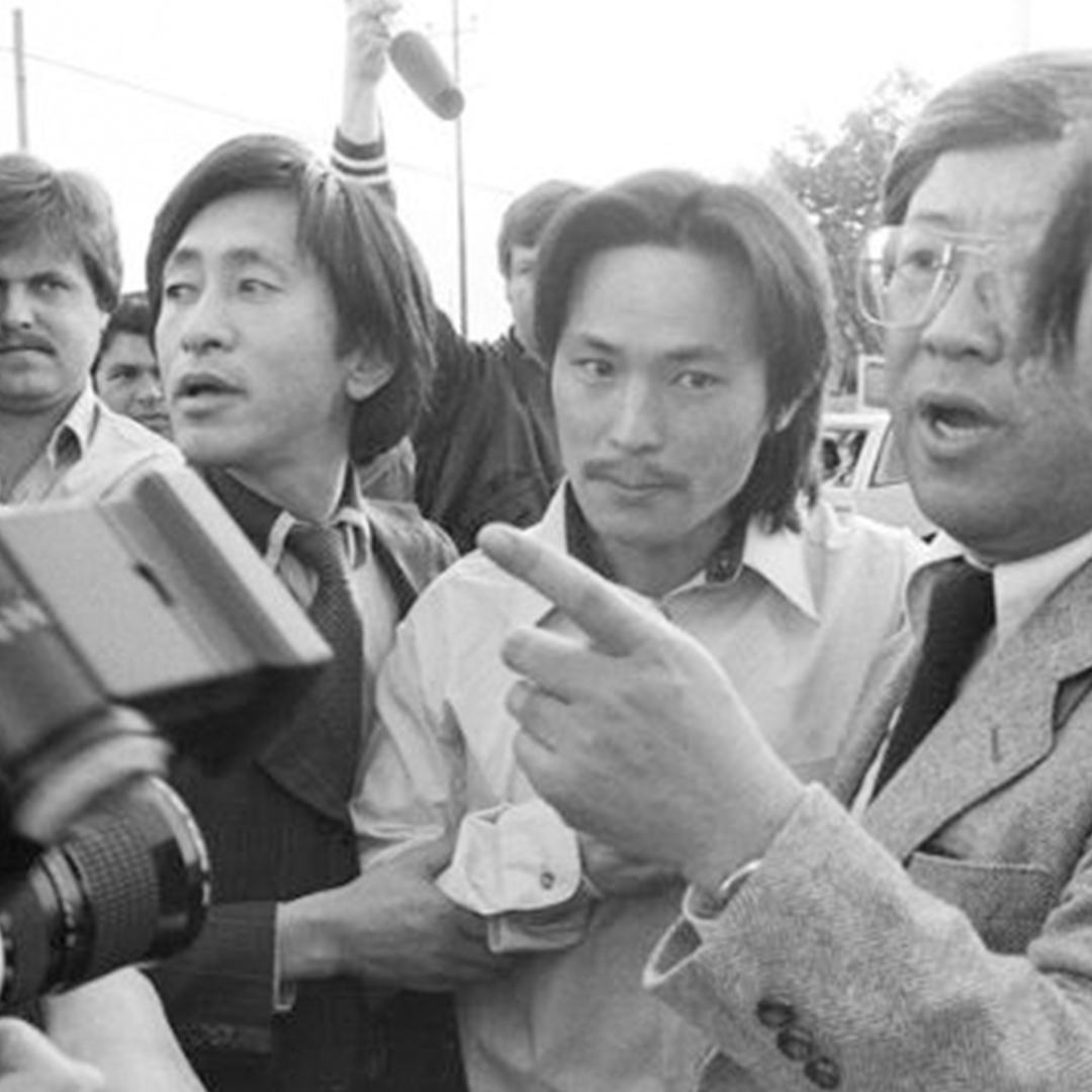 Black and white photograph of Korean immigrant Chol Soo Lee walking through a crowd of reporters.