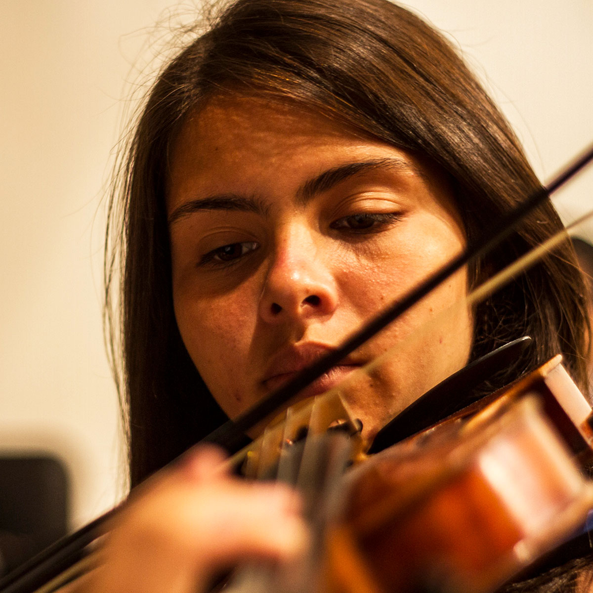 A close up of a young woman with light skin tone and dark hair playing the violin.