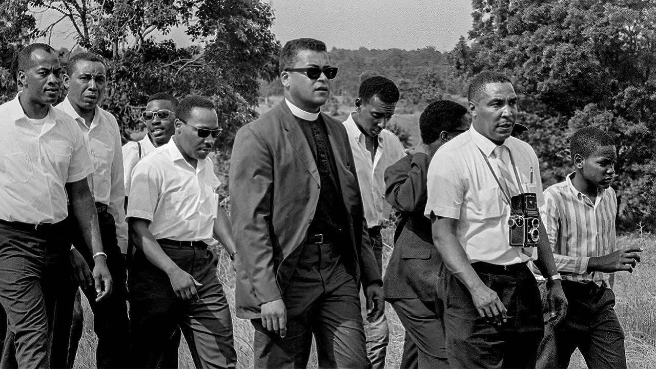 Black and white photograph of Black photographer Ernest Withers. He carries a camera while walking with a group of civil rights leaders.