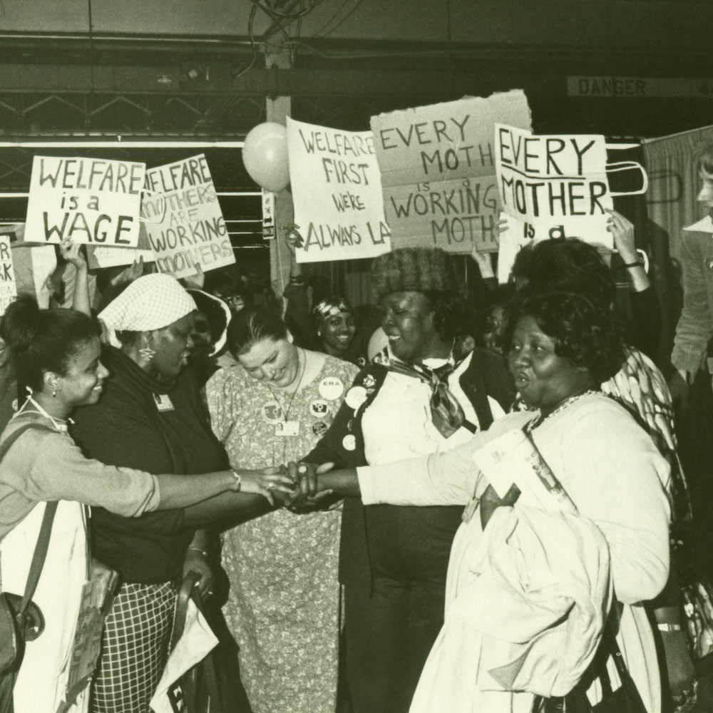 Credit: Diana Mara Henry Photography Caption: Welfare rights leaders (including Johnnie Tillmon and Beaulah Sanders) put their hands together, celebrating passage of their National Plan of Action item at the First National Women's Conference in Houston, Texas.