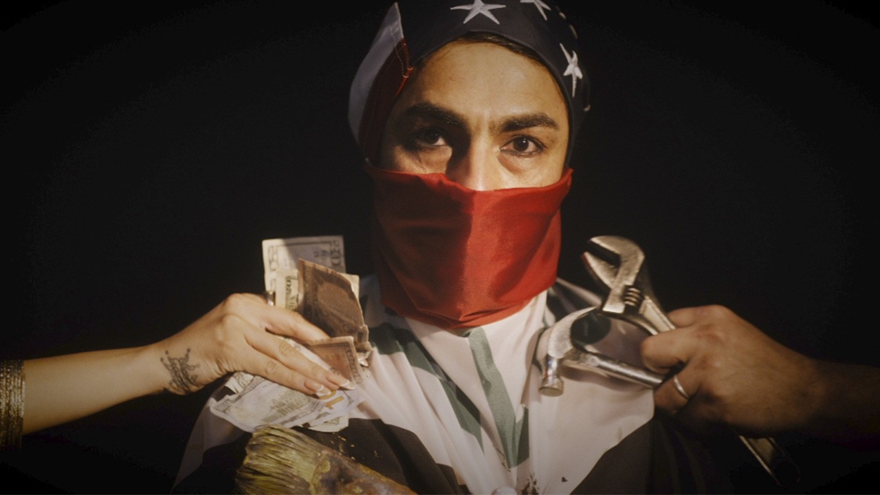 A man wears an American flag wrapped around his head and face with only his eyes showing. Two sets of hands surround him, carrying a hammer and wrench and American dollars, respectively.