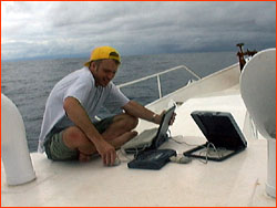 Mark attempting to transmit, via laptop and satphone, from deck of Orca