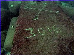 Block underwater with compass rose marked by divers in algae covering